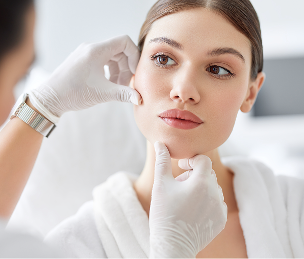 A clinician in white gloves gently examining a woman's face and jawline during a skin assessment.