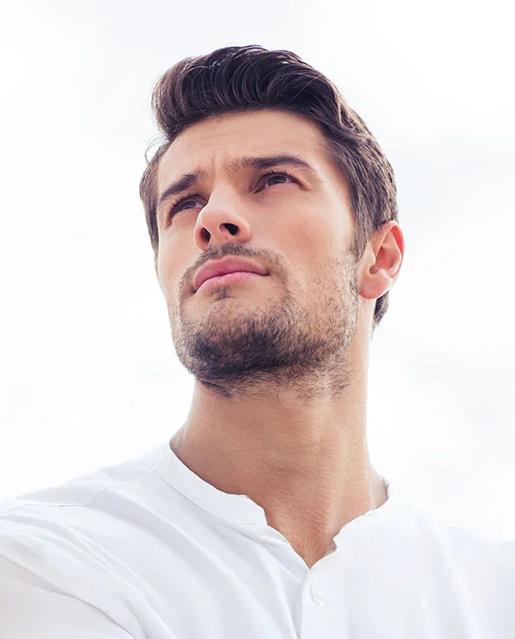 Close-up, low-angle shot of a handsome man in a white sweater looking upward, highlighting his brow and forehead area. - Facial Contouring in Hermosa Beach, CA