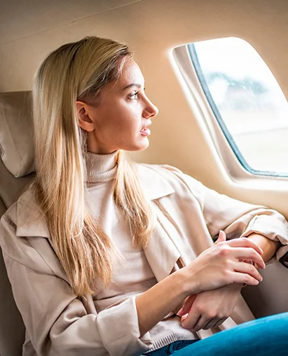 A woman with long blonde hair sits in an airplane seat and looks out the window. - Out of Town in Hermosa Beach, CA