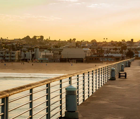 Shot of a long beach pier leading toward a coastal town under the golden light of a sunset. - Out of Town Recovery in Hermosa Beach, CA