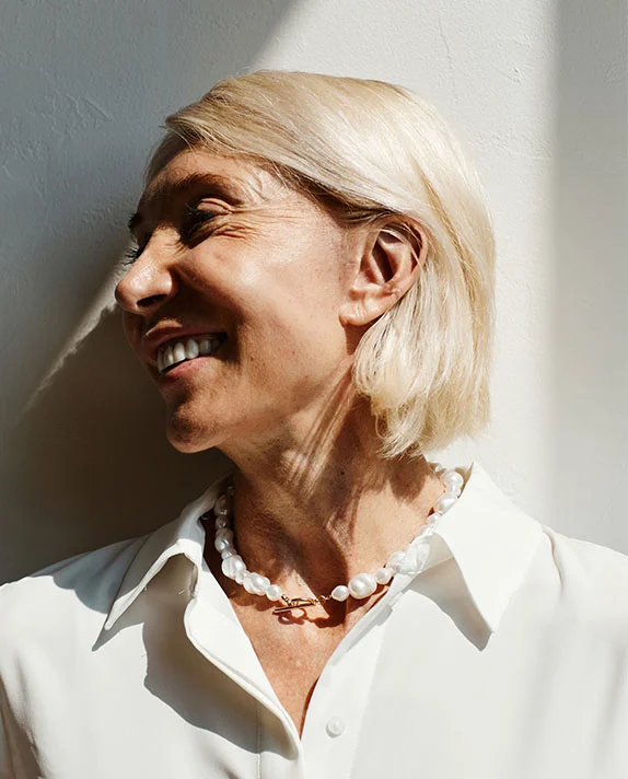 Profile view of a smiling older woman with blonde hair and a pearl necklace standing in bright sunlight. - Rhinopyma Correction in Hermosa Beach, CA